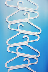 White Clothes hangers as creative minimal composition on soft blue gradient background, Plastic racks creating modern and geometric aesthetic, top view, flat lay creative photo, smooth lines pattern