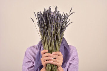 Mature woman with scarf on her head holding and covering her face with bouquet of lavender flowers