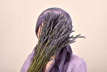 Mature woman with scarf on her head holding and covering her face with bouquet of lavender flowers
