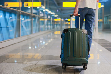Lower half of a traveler walking through an empty airport terminal, pulling a suitcase. The scene...