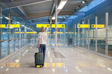 A young woman with a suitcase stands alone in an empty airport terminal, waiting for her flight....