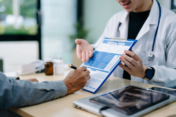Young Asian doctor explains medical form to senior male patient during a friendly consultation. Trust, care, and modern healthcare concep