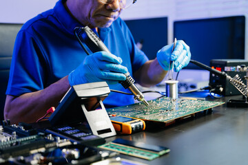 Senior technician soldering a circuit board on workbench. Blue gloves, precision tools, and...
