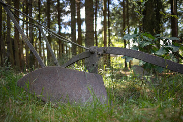 A rusty old plow is sitting in the grass in a forest