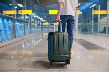 Lower half of a traveler walking through an empty airport terminal, pulling a suitcase. The scene...