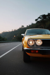 Fototapeta premium Vintage yellow sports car parked in urban street at dusk, close-up front headlight view of retro vehicle