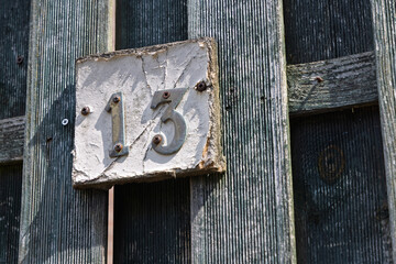 A rustic, weathered house number '13' on a distressed wooden fence, full of character.