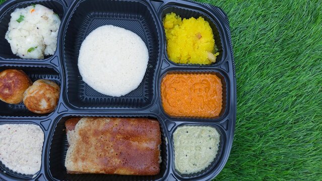 Traditional south Indian breakfast combo consisting of mini Benne dosa, paddu, idli, sheera and three type of chutneys on green grass background