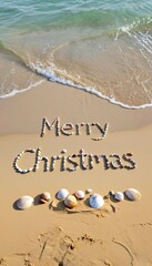 Text 'Merry Christmas' arranged with seashells on a sandy beach. Gentle waves lap at the shore, creating a holiday atmosphere.