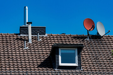 Bright sunlight highlights a rooftop with satellite antennas and a chimney. The clear blue sky...