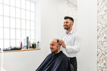 Hairdresser checking the fit of a hair replacement system on a smiling man in a hair salon,...