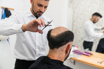 Fototapeta premium Hairdresser cutting remaining hair of customer in preparation for applying hair prosthesis in hair clinic