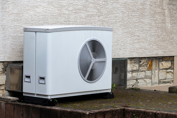 An air conditioning unit is situated outside a building on a hard surface. The unit has a large fan...