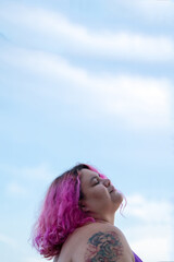 Woman with pink hair standing with eyes closed against the blue sky