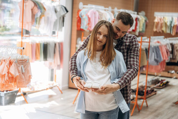 Pregnant woman with man are in the kid's clothing store