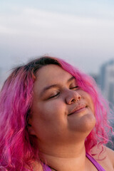 Woman with pink hair standing with eyes closed against the blue sky