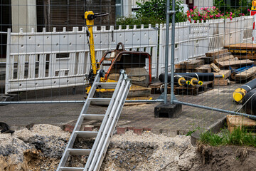 A construction site features a ladder leaning against a fenced area. Nearby, various equipment and...