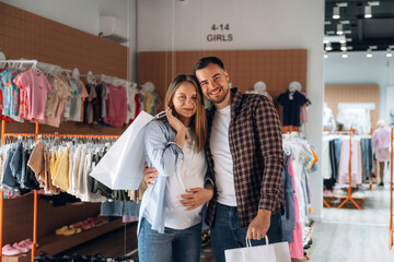 Shopping bags in hands. Pregnant woman with man are in the kid's clothing store