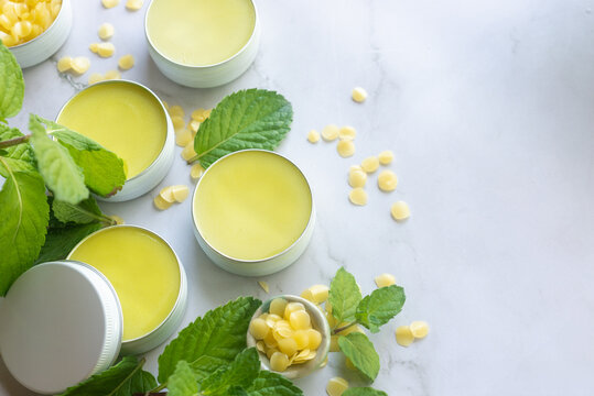 homemade fresh mint balm salve in reusable white tin with fresh mint leaves on white marble background.