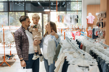 Asking if child like that wear. Father, son and pregnant mother are in kid's clothing store