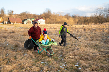 Family bonding during a late afternoon in the countryside with a joyful child in a wheelbarrow and adults engaging in outdoor activities