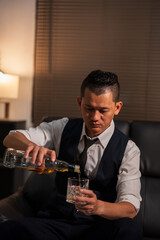 Businessman holding a glass of whiskey and drinking on a sofa.