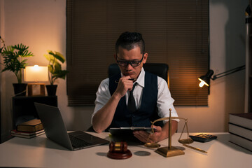 Male lawyer is sitting at work, using a laptop, and has legal books on his desk.