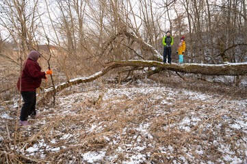 Winter adventure unfolds in a snowy landscape where friends explore nature while one person carefully climbs a fallen tree under the watchful eye of their companions