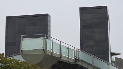 Fototapeta premium Two tall rectangular towers connected by a raised pedestrian walkway with frosted glass railing.