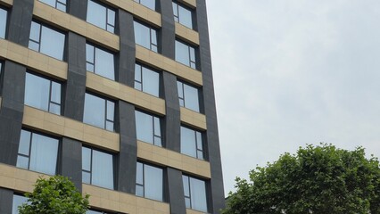 A partial view of a modern office building with clean vertical lines and reflective windows next to green trees.