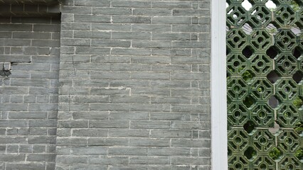 Close-up of a traditional Chinese gray brick wall with an ornate green lattice window on the side.