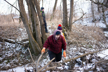 Group of people navigating a snowy landscape while collecting branches for firewood alongside a wooden creek in a tranquil, wintry setting