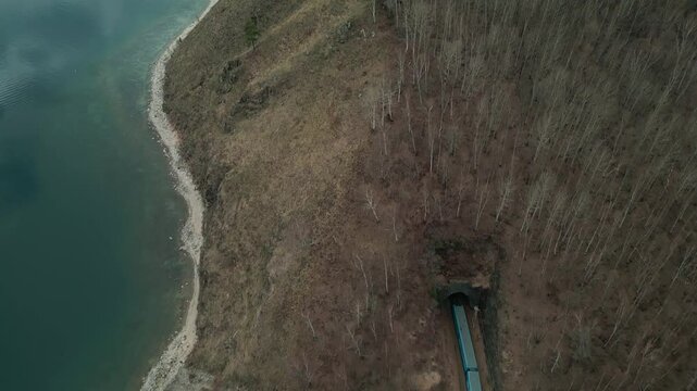 A spring landscape of Lake Baikal with a view of clearwater and a railway with a train at the foot of the hills