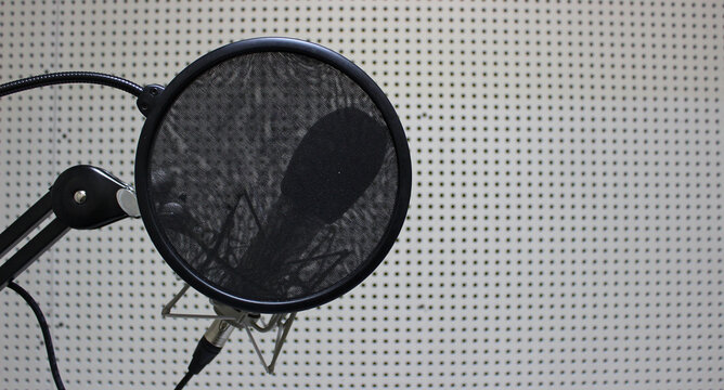 A round cloth pop filter in front of a microphone for reading text in a studio 