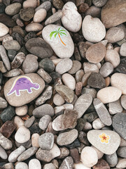 Pebbles with drawings of palm and dinosaur
