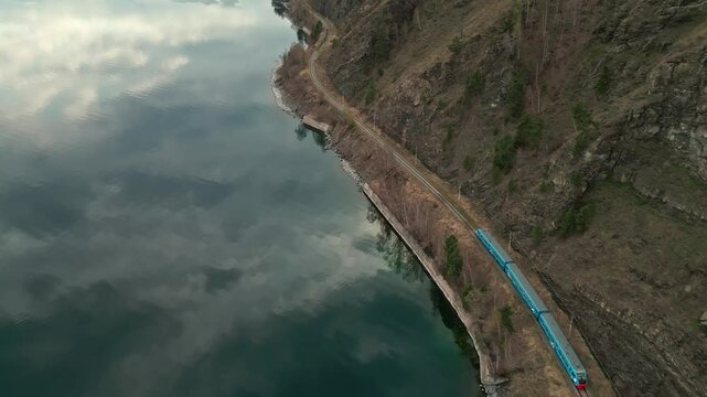A spring landscape of Lake Baikal with a view of clearwater and a railway with a train at the foot of the hills