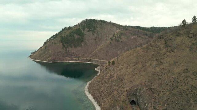 A spring landscape of Lake Baikal with a view of clearwater and a railway with a train at the foot of the hills