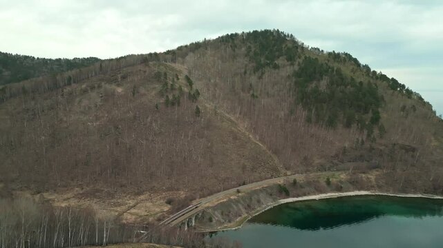 A spring landscape of Lake Baikal with a view of clearwater and a railway with a train at the foot of the hills