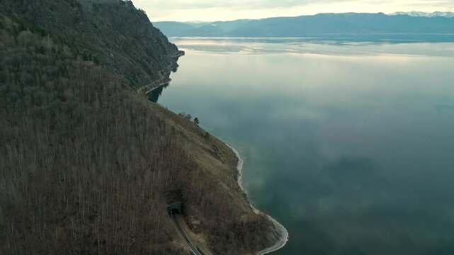 A spring landscape of Lake Baikal with a view of clearwater and a railway with a train at the foot of the hills