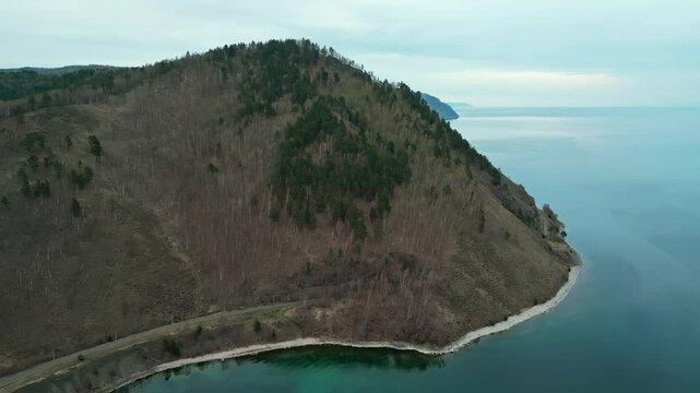 A spring landscape of Lake Baikal with a view of clearwater and a railway with a train at the foot of the hills