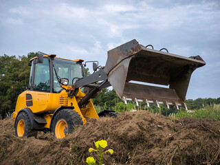 Carregadeira de rodas a trabalhar no espalhamento de terra em meio a uma fazenda agrícola para a construção de um caminho num dia nublado