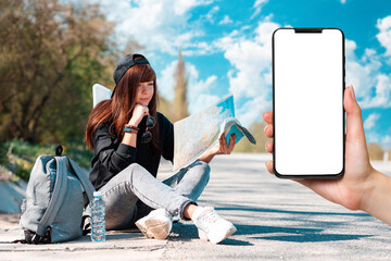 Hitchhiking. Young smiling woman in cap sitting along the road and looking at paper map. Female...