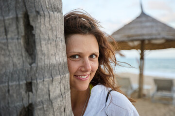 A happy woman smiles, touching her cheek to a palm tree.
