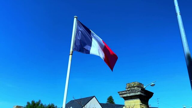 French flag slowly unfurling in the wind against a blue sky to show the full flag