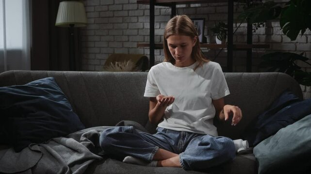 Young Woman Sitting on Couch Holding Pills Thoughtfully