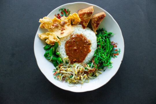 Nasi Pecel or sego pecel is Traditional Javanese rice dish of steamed rice with vegetable salad, peanut sauce, tempeh, tofu bean sprouts and crackers or peyek kacang. on black backgroud