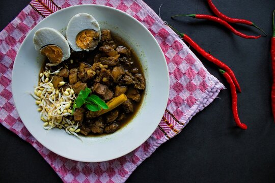 Rawon or Nasi Rawon/Rawon Rice is traditional Indonesian beef black soup served with sprouts, salted eggs, kluwek seasoning. From east java. Isolated on black background