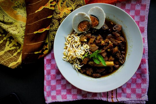Rawon or Nasi Rawon/Rawon Rice is traditional Indonesian beef black soup served with sprouts, salted eggs, kluwek seasoning. From east java. Isolated on black background