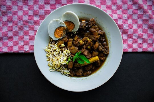 Rawon or Nasi Rawon/Rawon Rice is traditional Indonesian beef black soup served with sprouts, salted eggs, kluwek seasoning. From east java. Isolated on black background