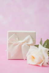 Closeup of elegant white gift box with satin ribbon and rose bouquet